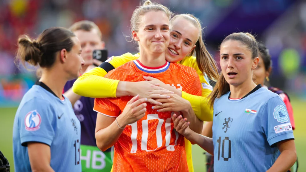 "Miedemazo" en una cita histórica para Gales. Vivianne Miedema, con una camiseta conmemorativa por su gol número 100, se abrazada por Daphne van Domselaar ante la atenta mirada de Danielle van de Donk.