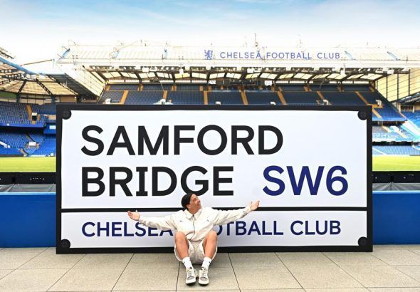 Sam se Kerrda. Sam Kerr posa en Stamford Bridge con una señal callejera tamaño XXL que reza: "SAMFORD BRIDGE".